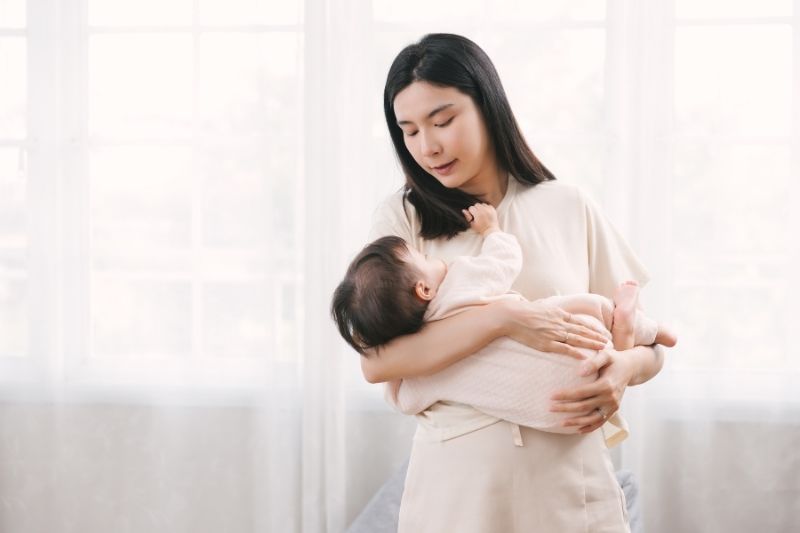 Mẹ trẻ ôm con trong vòng tay nhẹ nhàng, ánh mắt bình an