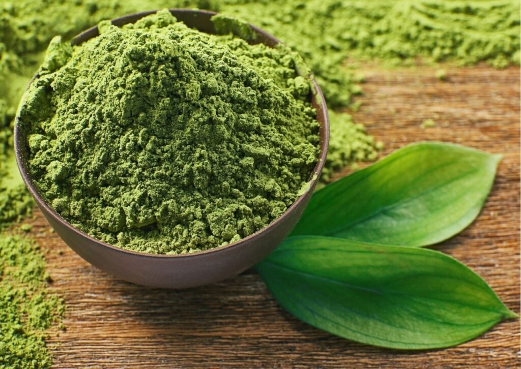 Bột matcha xanh tươi rắc trên bàn gỗ cùng lá trà.