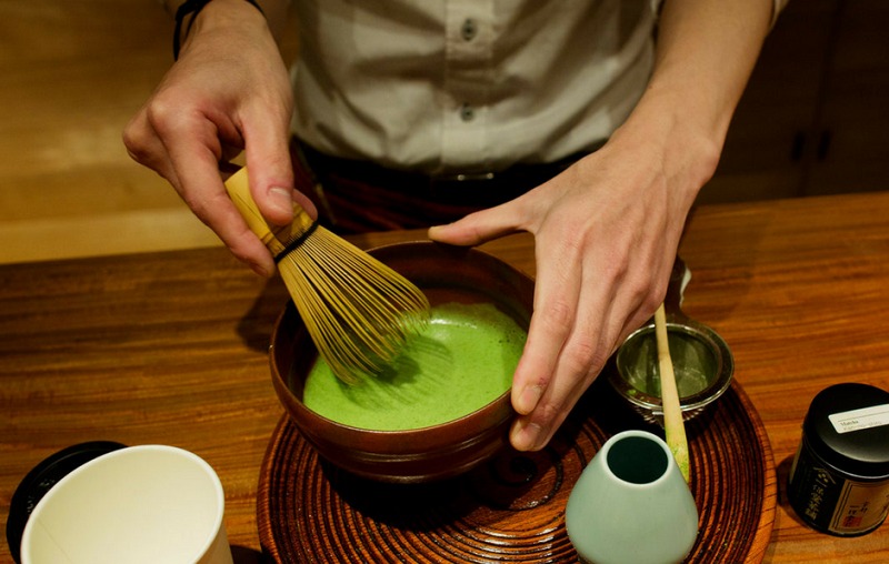 Người đánh trà matcha bằng chổi tre trong chén gốm.